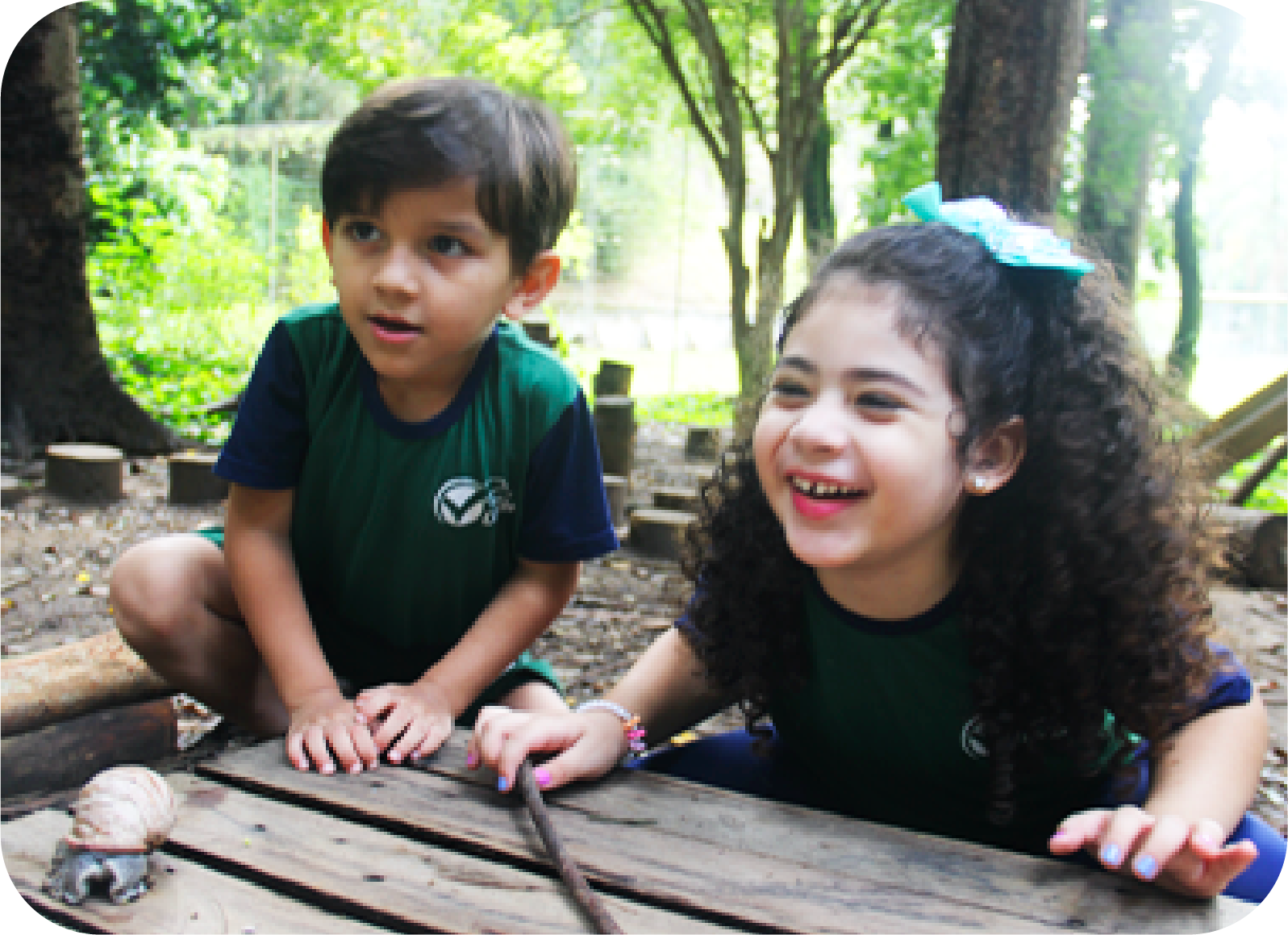Foto de duas crianças sorridentes brincando na 'floresta' com mandeira.